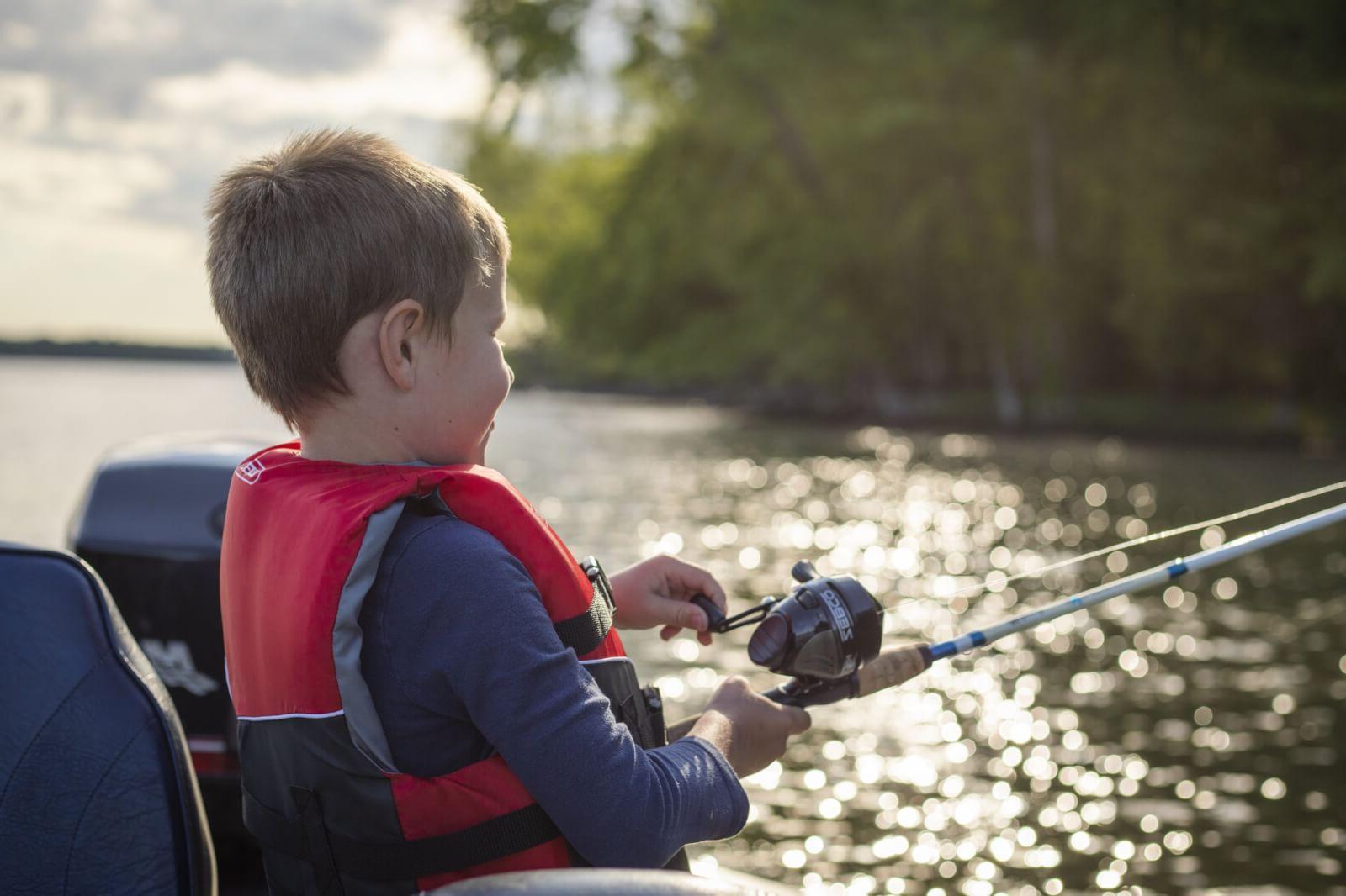 Young boy in a red vest holding a fishing rod and Fashioning on a lake